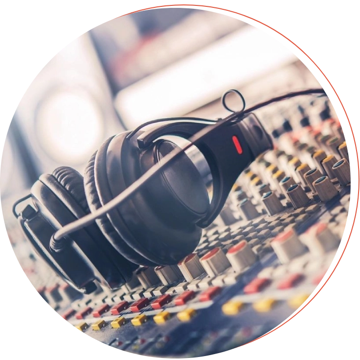 A pair of black headphones lies on a professional audio mixing console with various buttons and sliders.